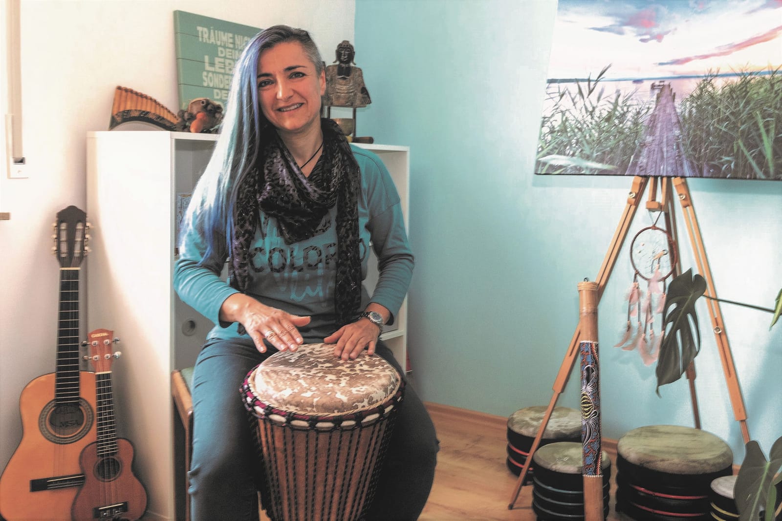 Biggi Käfer trommelt auf einer Djembe in ihrer Praxis, umgeben von Instrumenten
